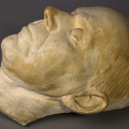 Photo of a white stone sculpture of a man's head, yellowed with age, lying face up on a black background.