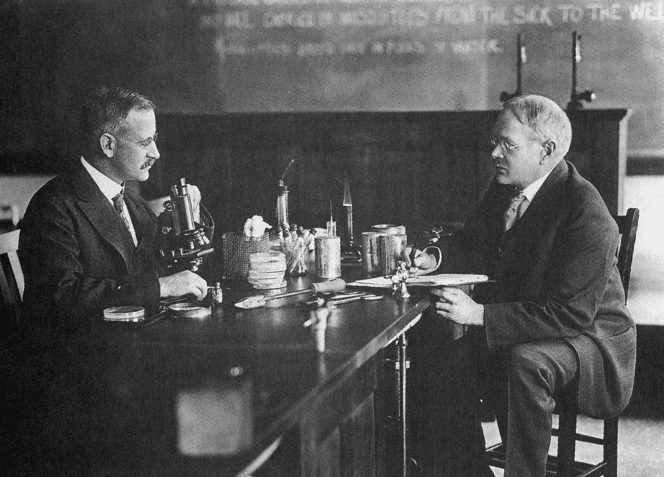 scan of black and white photo of two men sitting down at a table in discussion