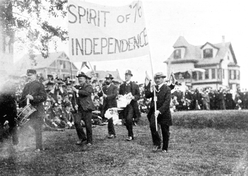 scan of black and white photo of men marching, two men holding a banner "Spirit of '76 Independence".