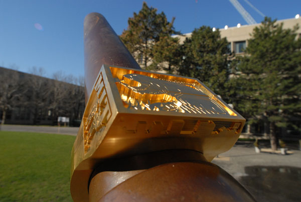 Photo of a giant brass rat being worn like the cannon is a finger, with MIT buildings in the background